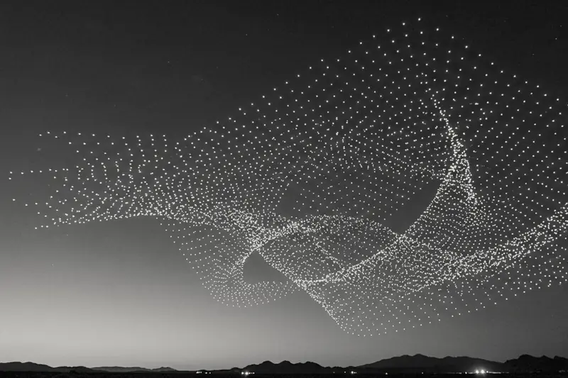 Hundreds of lit drones flying in formation over hills at dusk