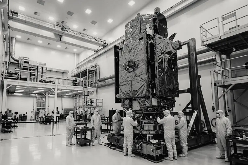 Technicians in cleanroom suits working on a large satellite